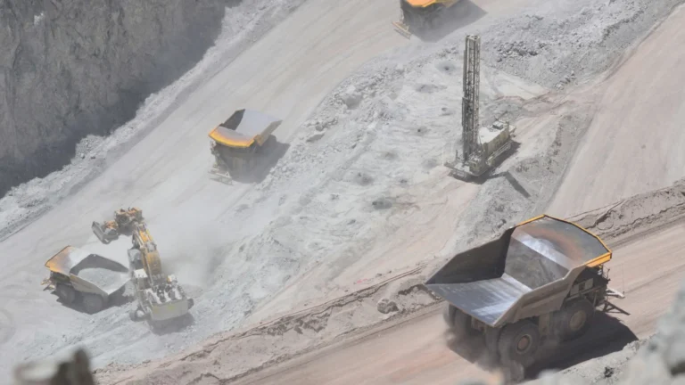 High-angle view of a large, active African open-pit mine featuring heavy yellow haul trucks transporting ore, with an excavator loading a truck on a terraced slope.