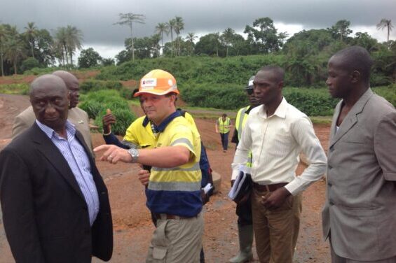 African Minerals Limited (AML) manager in a hard hat discussing mining operations with Sierra Leone community leaders near the Tonkolili Project site.