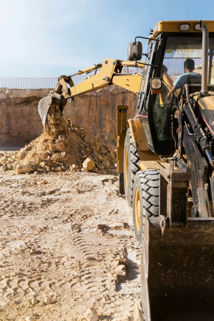 Backhoe loader excavating earth, symbolizing AMML's active investment in West African mining and construction development.