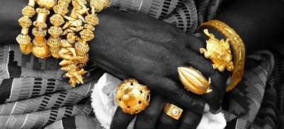 Professional woman holding a tray of finished gold items (jewelry/coins), representing the high-value end of AMML Sierra Leone's gold investment portfolio.